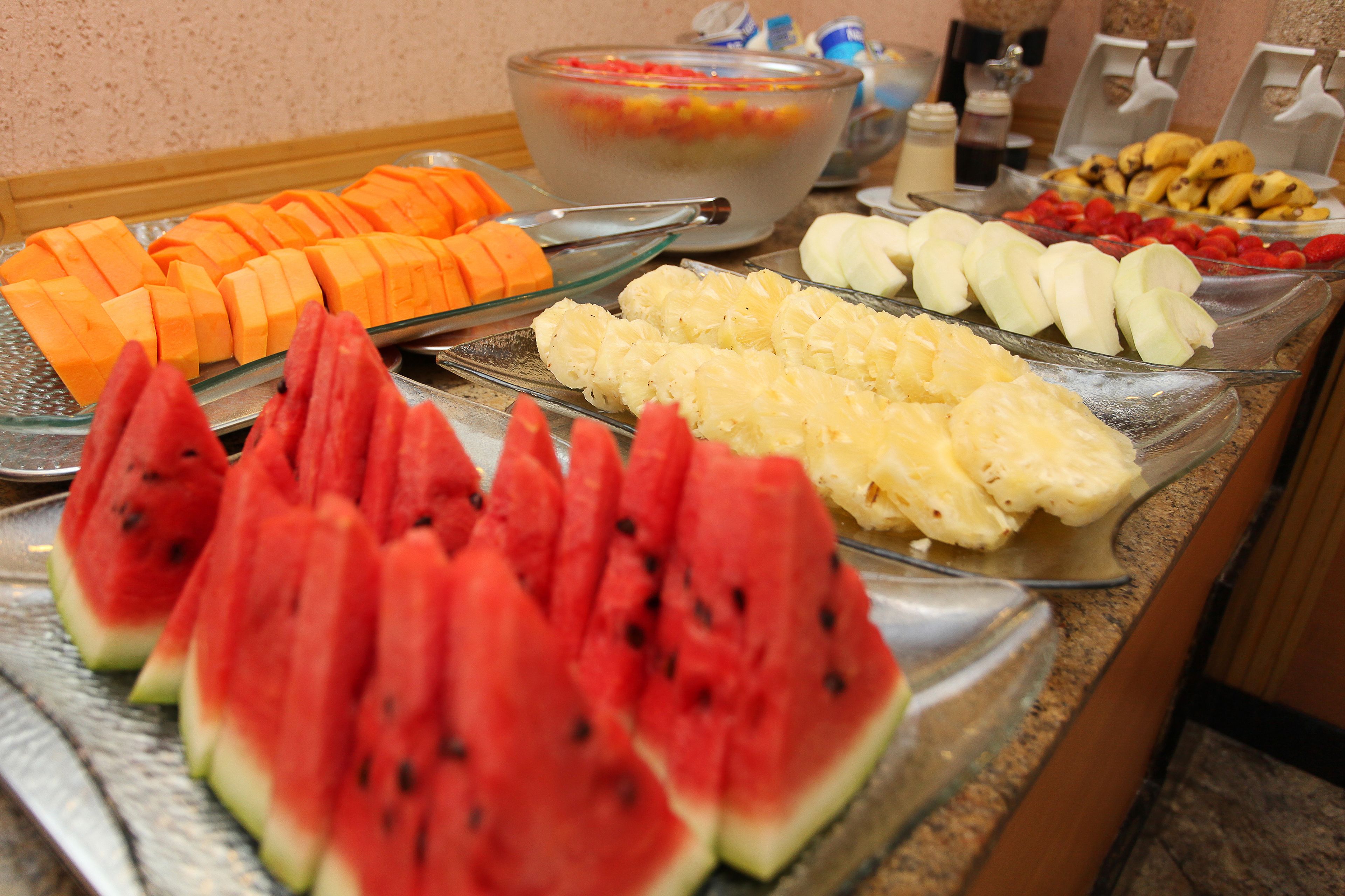 Un bufé con diversas frutas y un tazón grande de ensalada de frutas mixtas.