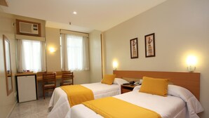 A hotel room with two beds, a desk, a chair, a small refrigerator, and two wall-mounted lights. - Hotel Vermont Ipanema (Rio de Janeiro)