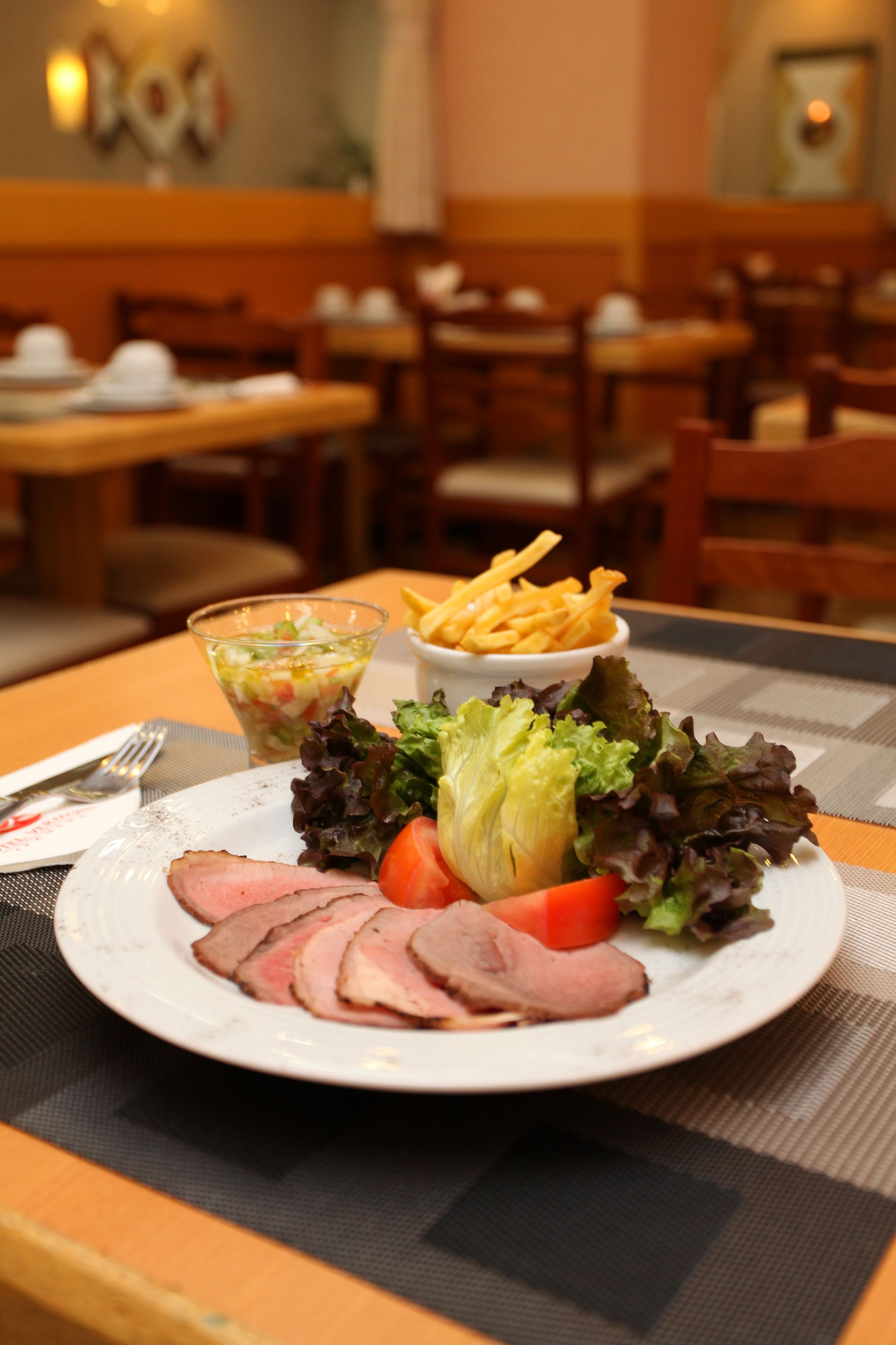 A dining table with a plate of food, including sliced meat, vegetables, and a small bowl of fries.