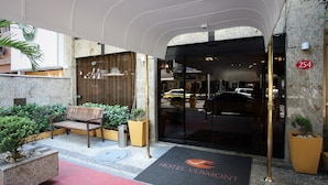 A hotel entrance with a red carpet, a wooden bench, potted plants, and a clear glass door. - Hotel Vermont Ipanema (Rio de Janeiro)