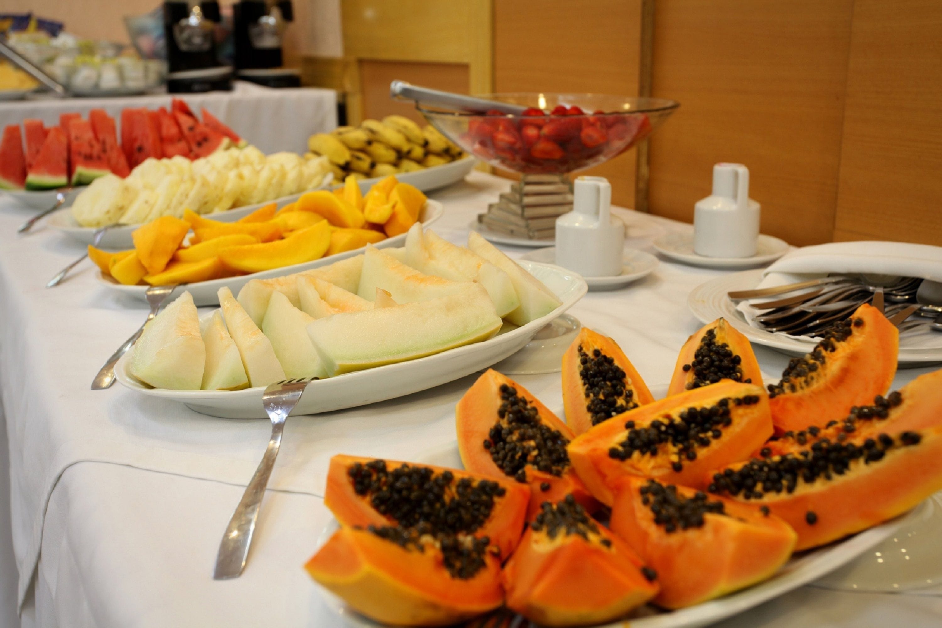 Een buffettafel met diverse soorten fruit, waaronder watermeloen, bananen, mango's, meloen en papaja.