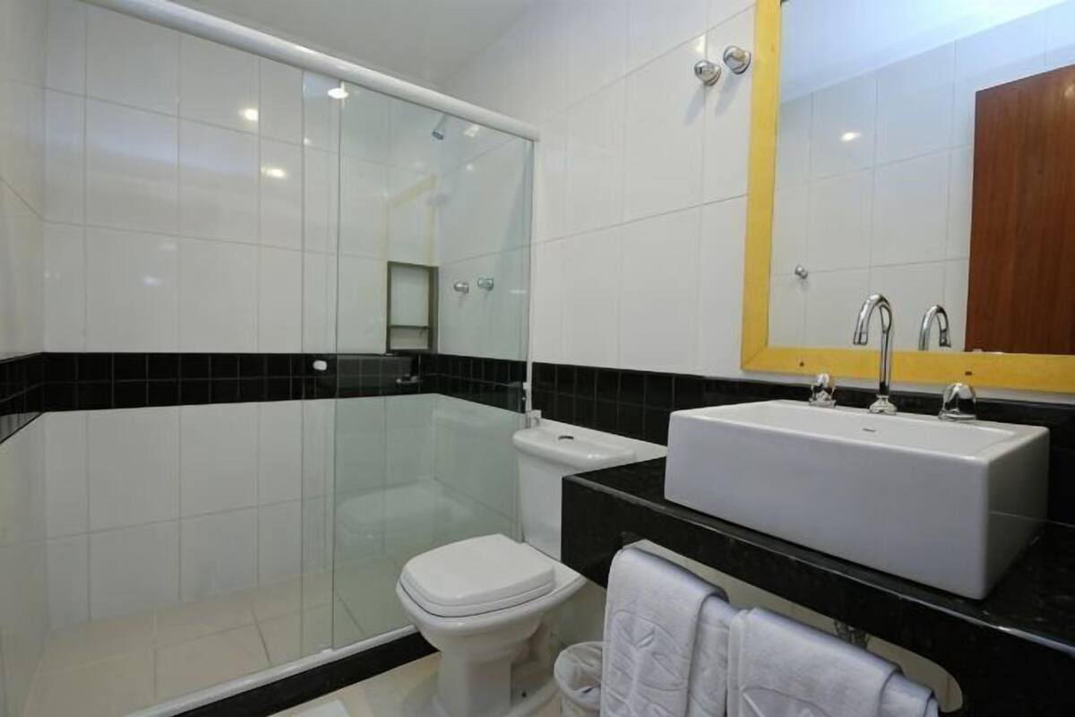 Een moderne badkamer met een douchecabine van glas, een wit toilet, een wastafel met spiegel en een handdoekrek.