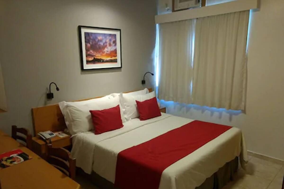 A hotel room with a bed, a nightstand, a desk, and a window with curtains.