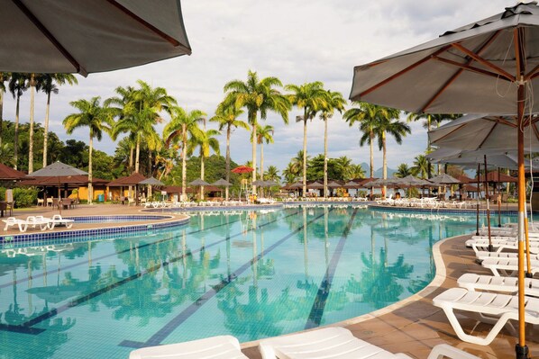 A pool with lounge chairs and umbrellas, surrounded by palm trees. - Vila Gale Angra - All Inclusive (Angra dos Reis)