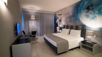 Quarto de hotel moderno com uma cama grande, uma escrivaninha, uma cadeira, uma televisão e um mural na parede.