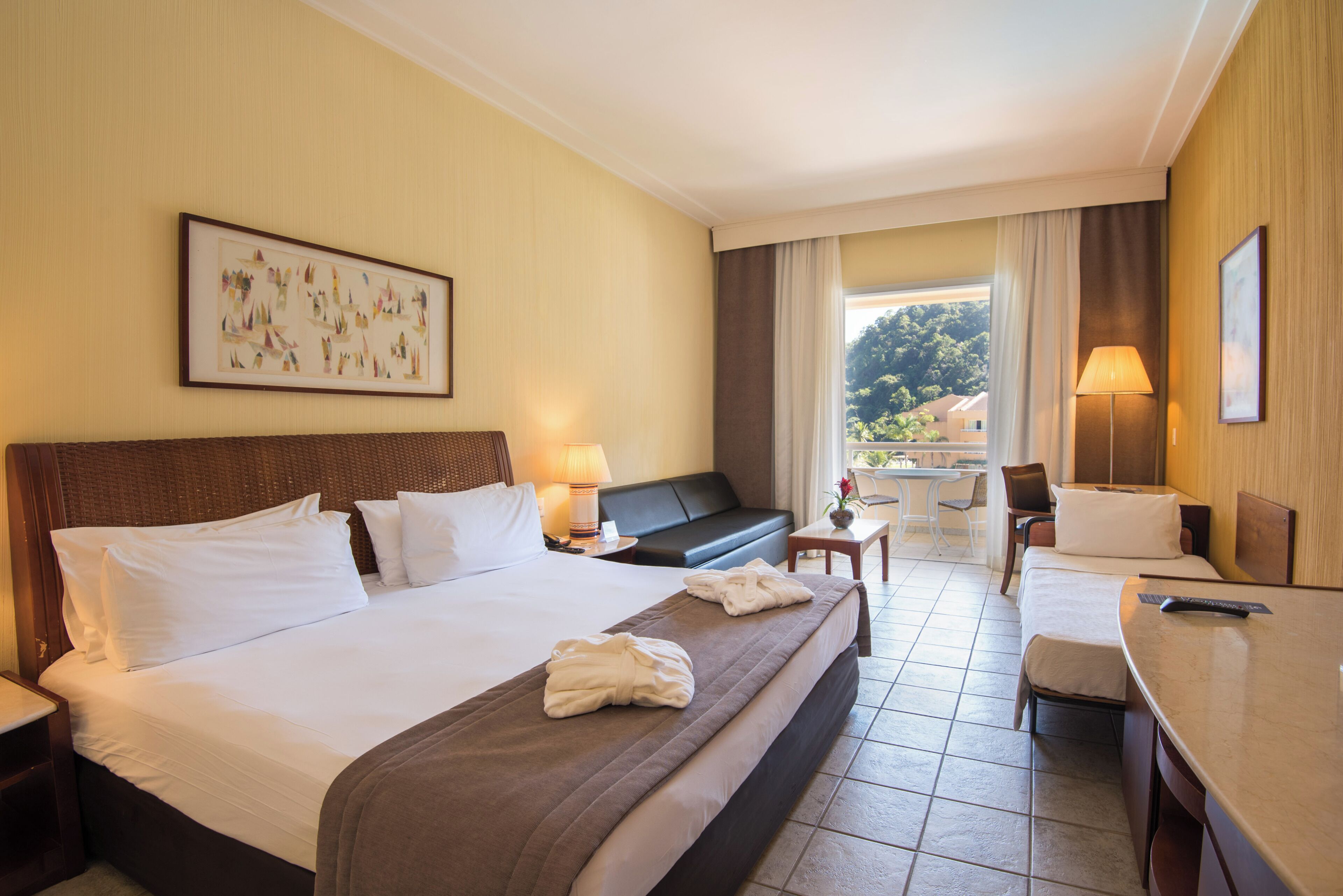 A hotel room with a large bed, a sofa, a desk, and a view of the outdoors.