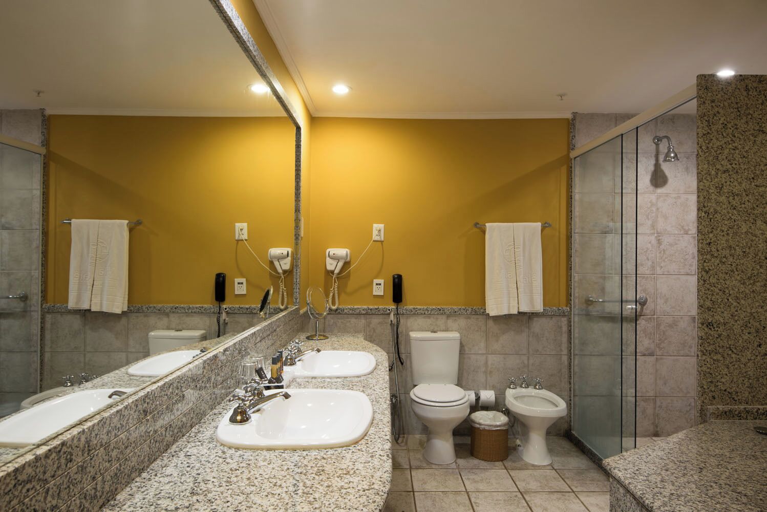Un baño con un espejo grande, dos lavamanos, un inodoro y una ducha.