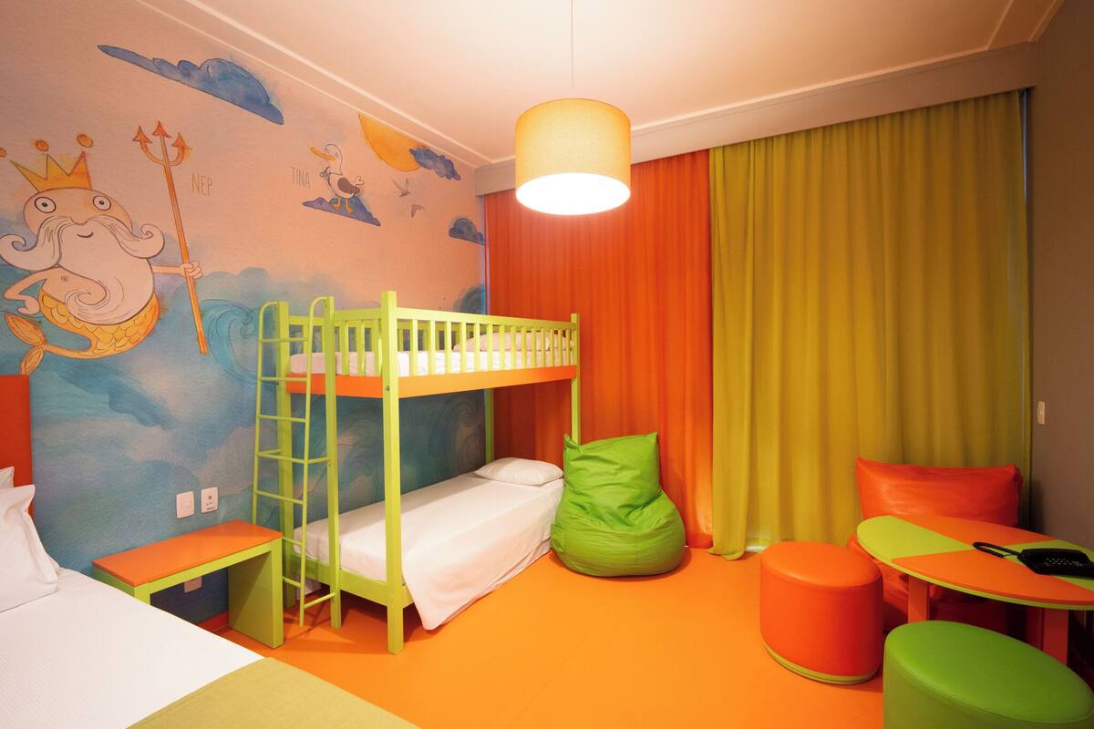 A child's room with bunk beds, a green bean bag chair, a small table, and a mural on the wall.