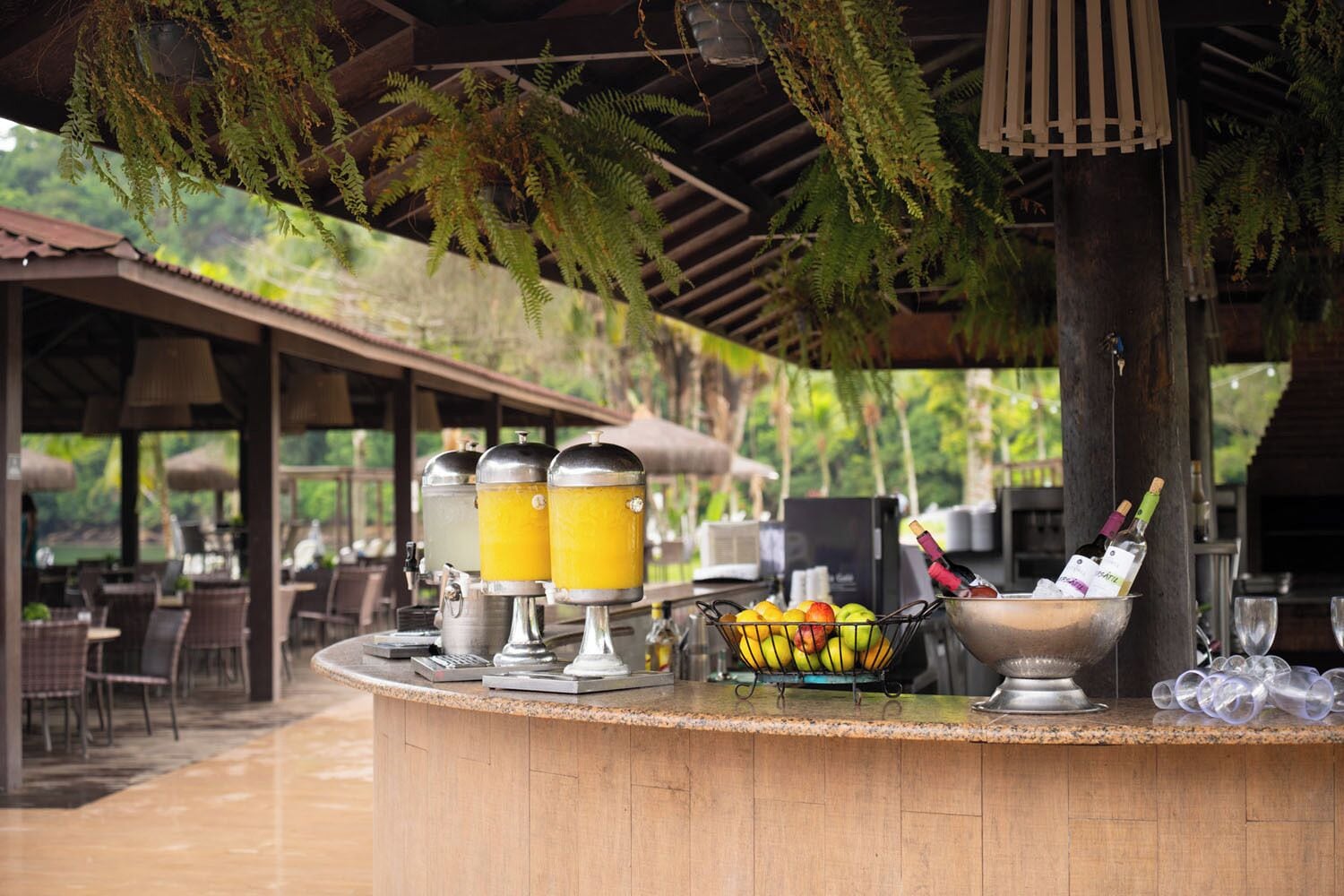 A bar area with a drink dispenser, fruit bowl, and wine bottles.