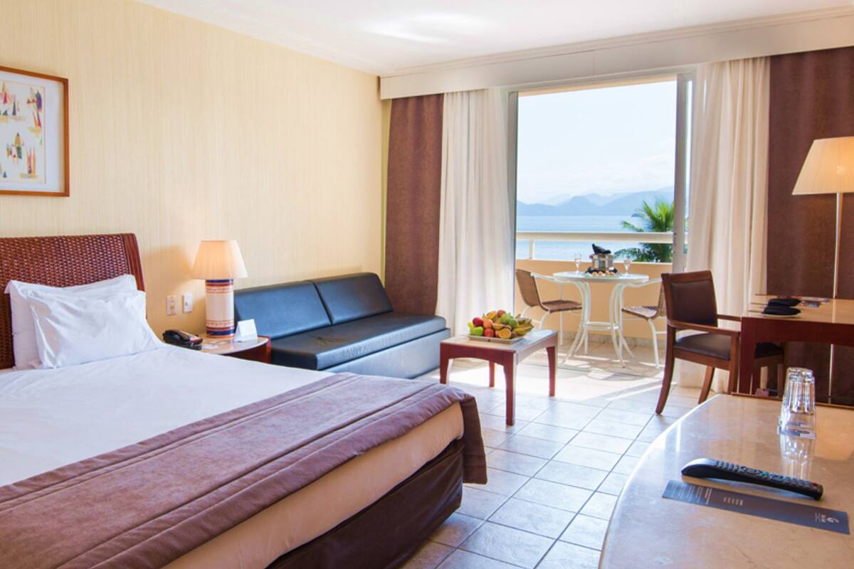 A hotel room with a large bed, a sofa, a desk, and a view of the sea.