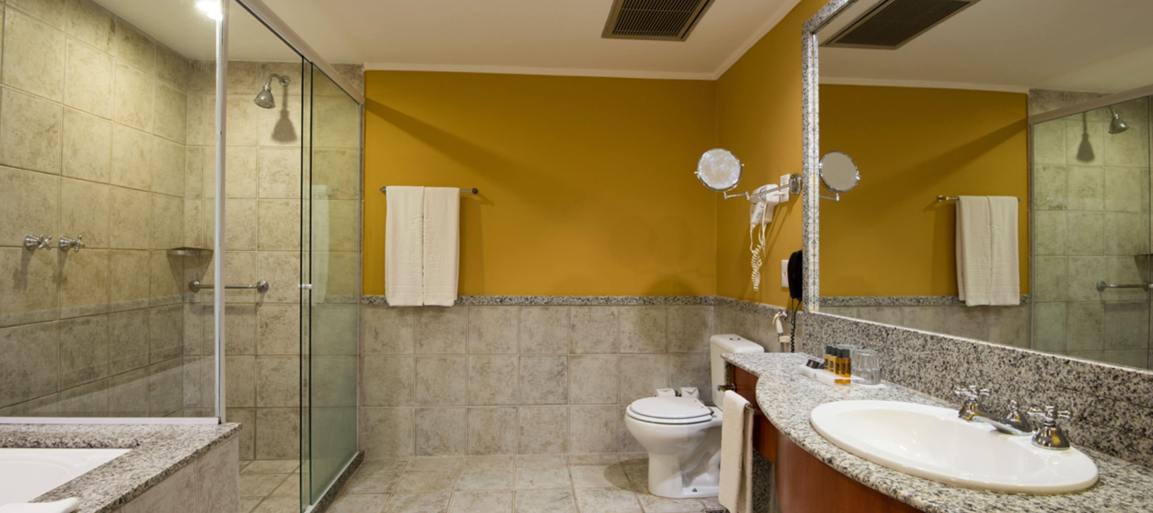 Un baño moderno con cabina de ducha de vidrio, un inodoro blanco, un lavamanos de granito y un espejo grande.