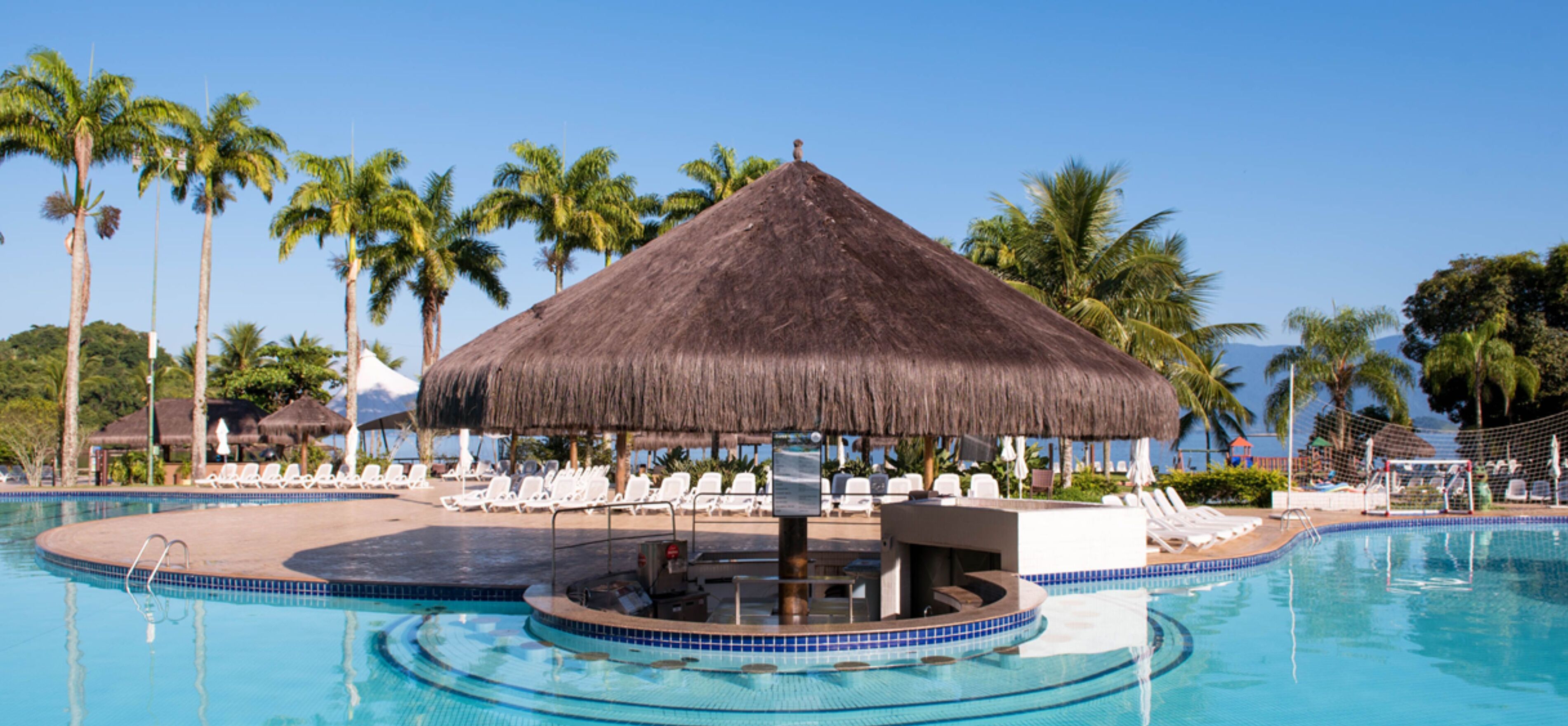 A pool area with a thatched-roof structure, lounge chairs, and palm trees.
