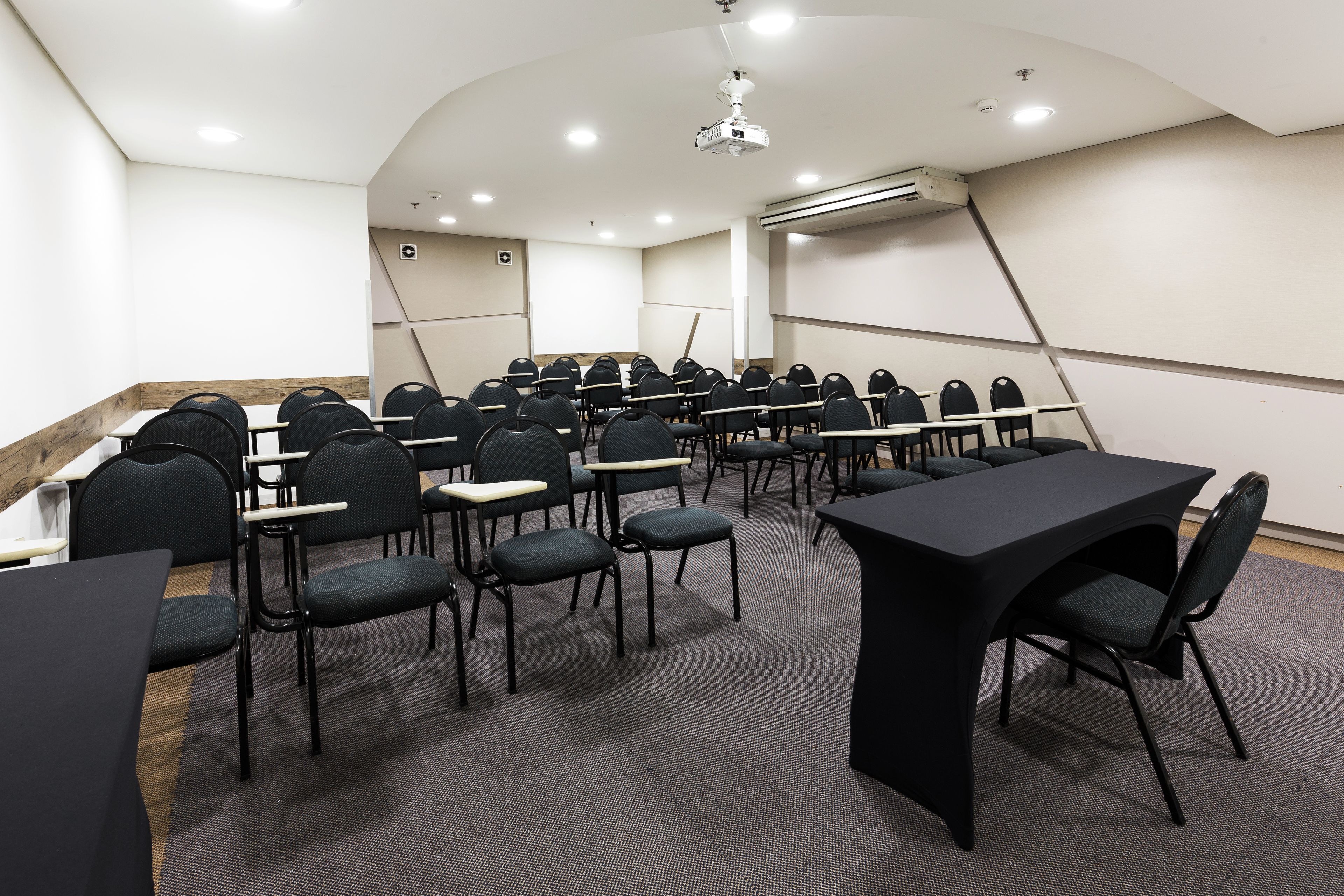 Un salón de conferencias con filas de sillas, mesas, un proyector y un equipo de aire acondicionado.