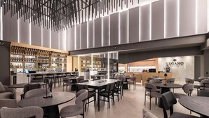 Un restaurante moderno con varias zonas de estar, incluidas mesas redondas y sofás, y una zona de bar con estantes llenos de botellas.