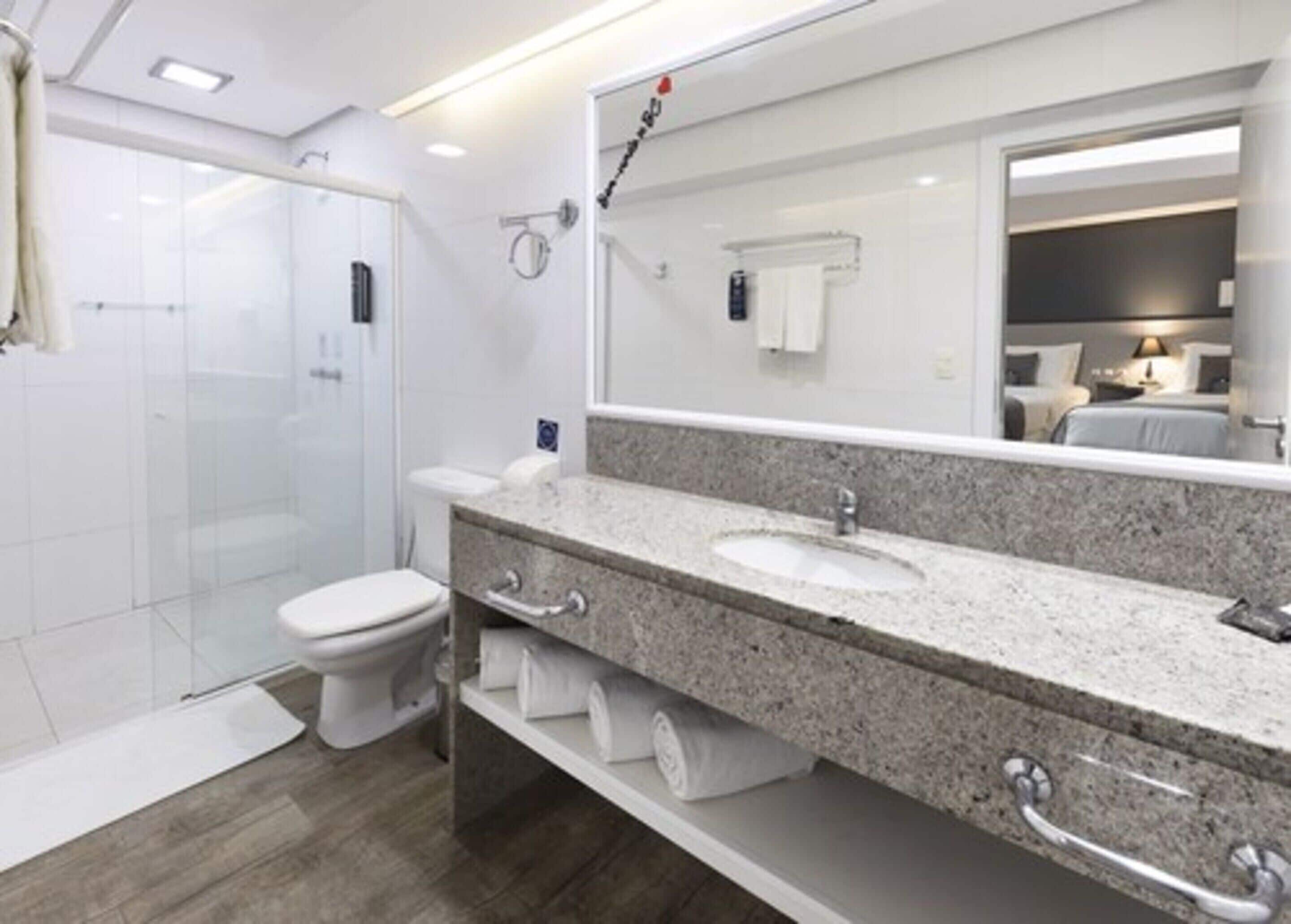 A modern bathroom with a glass shower enclosure, a white toilet, and a granite countertop with two sinks.