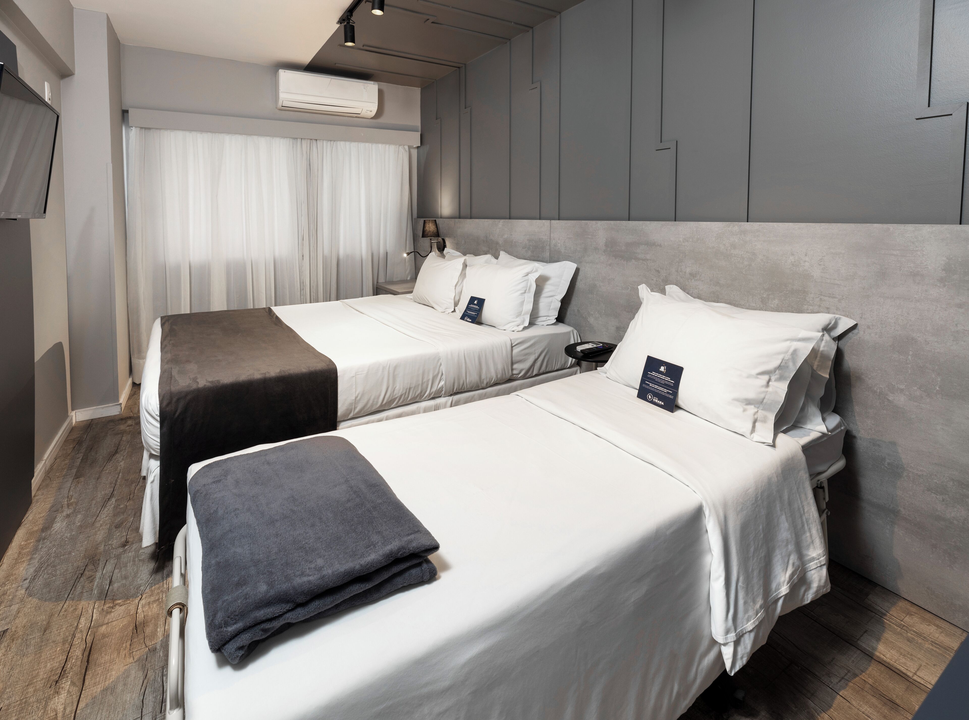 Habitación de hotel con dos camas, una mesita de noche, aire acondicionado y una ventana con cortinas.