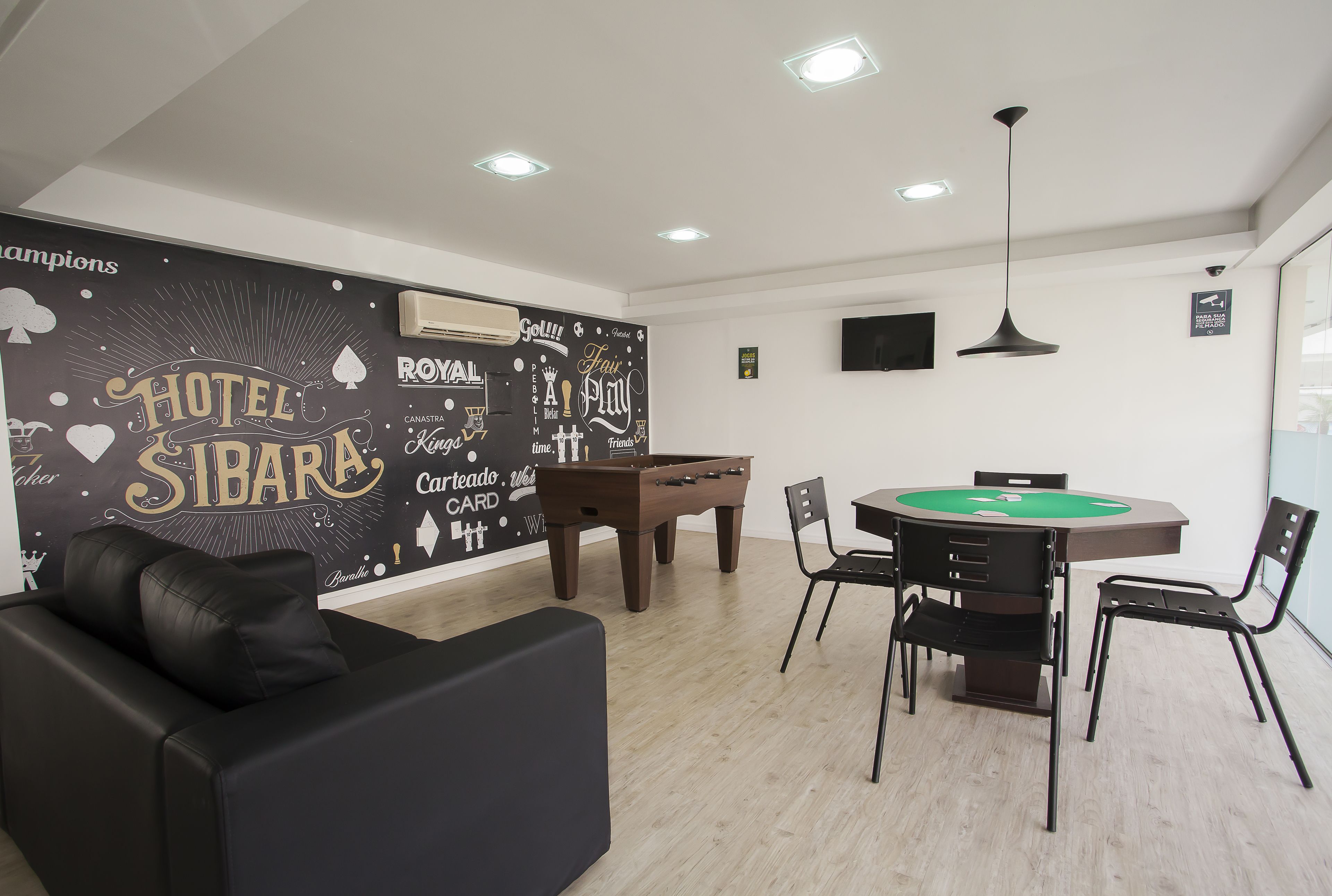 A modern hotel room with a pool table, a sofa, and a dining table with chairs.