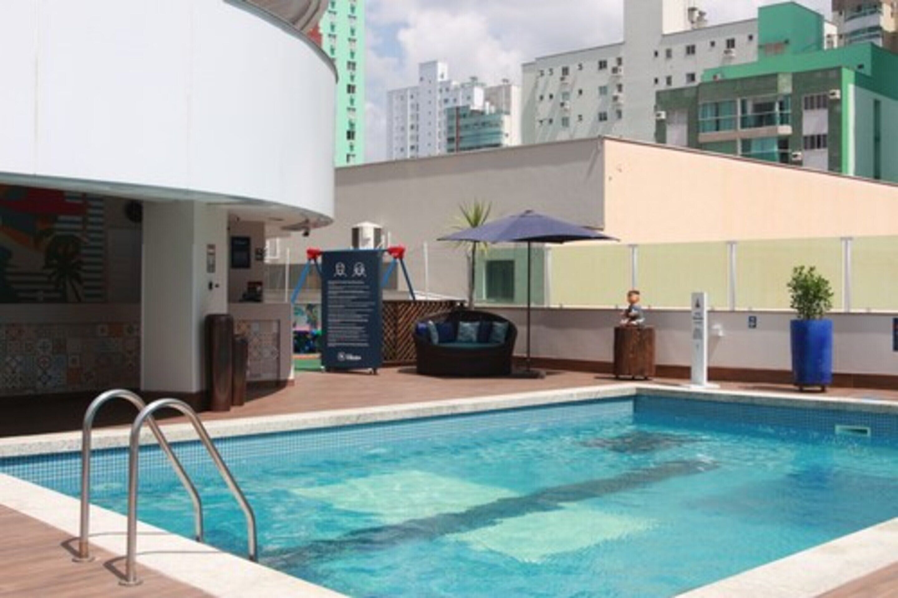 A swimming pool with a lounge area, a hot tub, and a view of the cityscape.