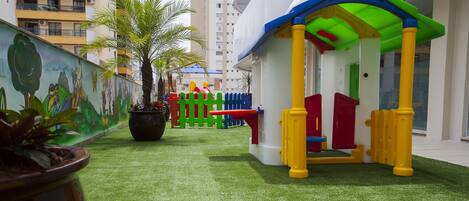 A children's play area with a small playhouse, a mural, and a palm tree.