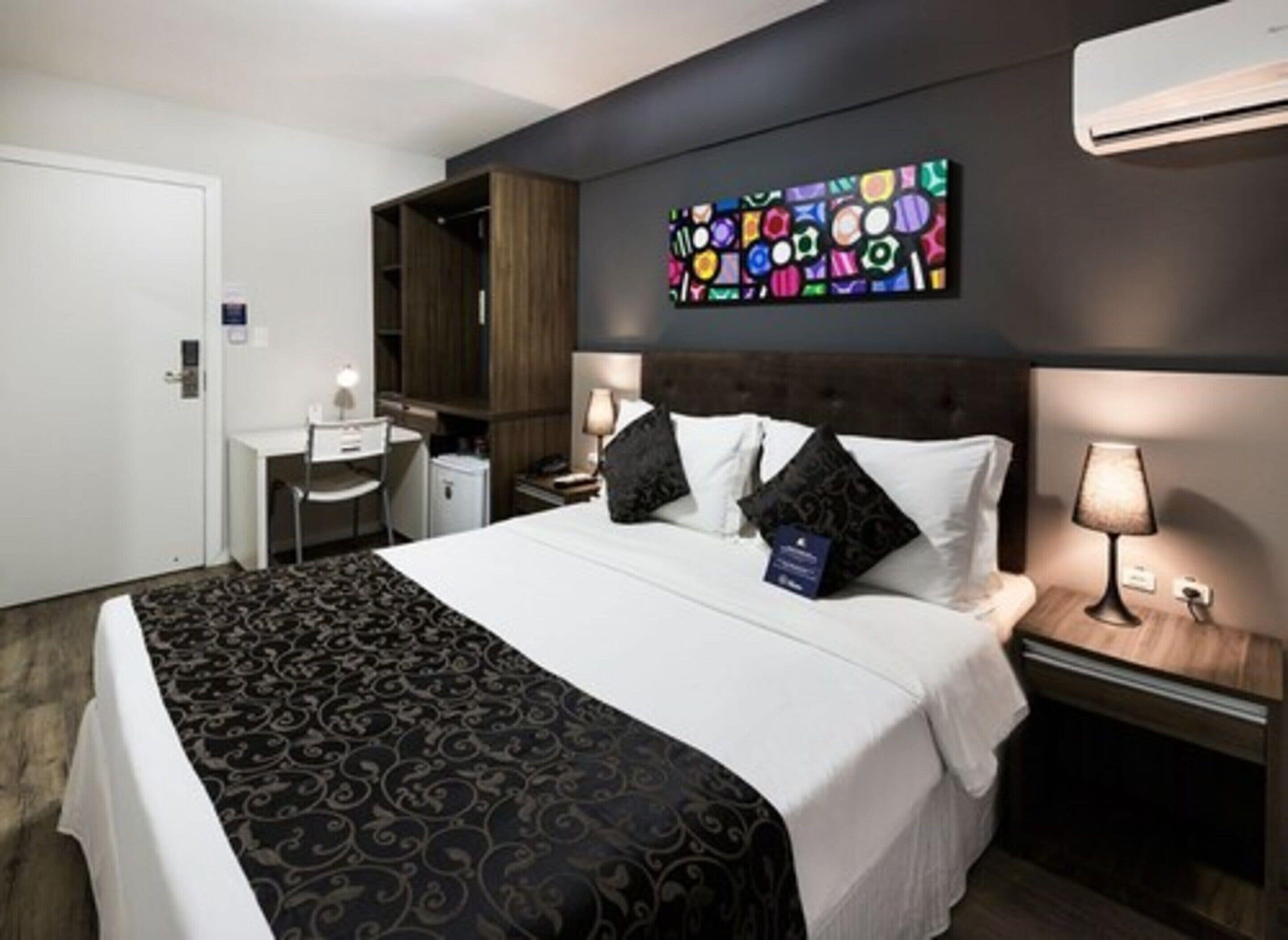 Una habitación de hotel con una cama, mesitas de noche, un escritorio y un armario.