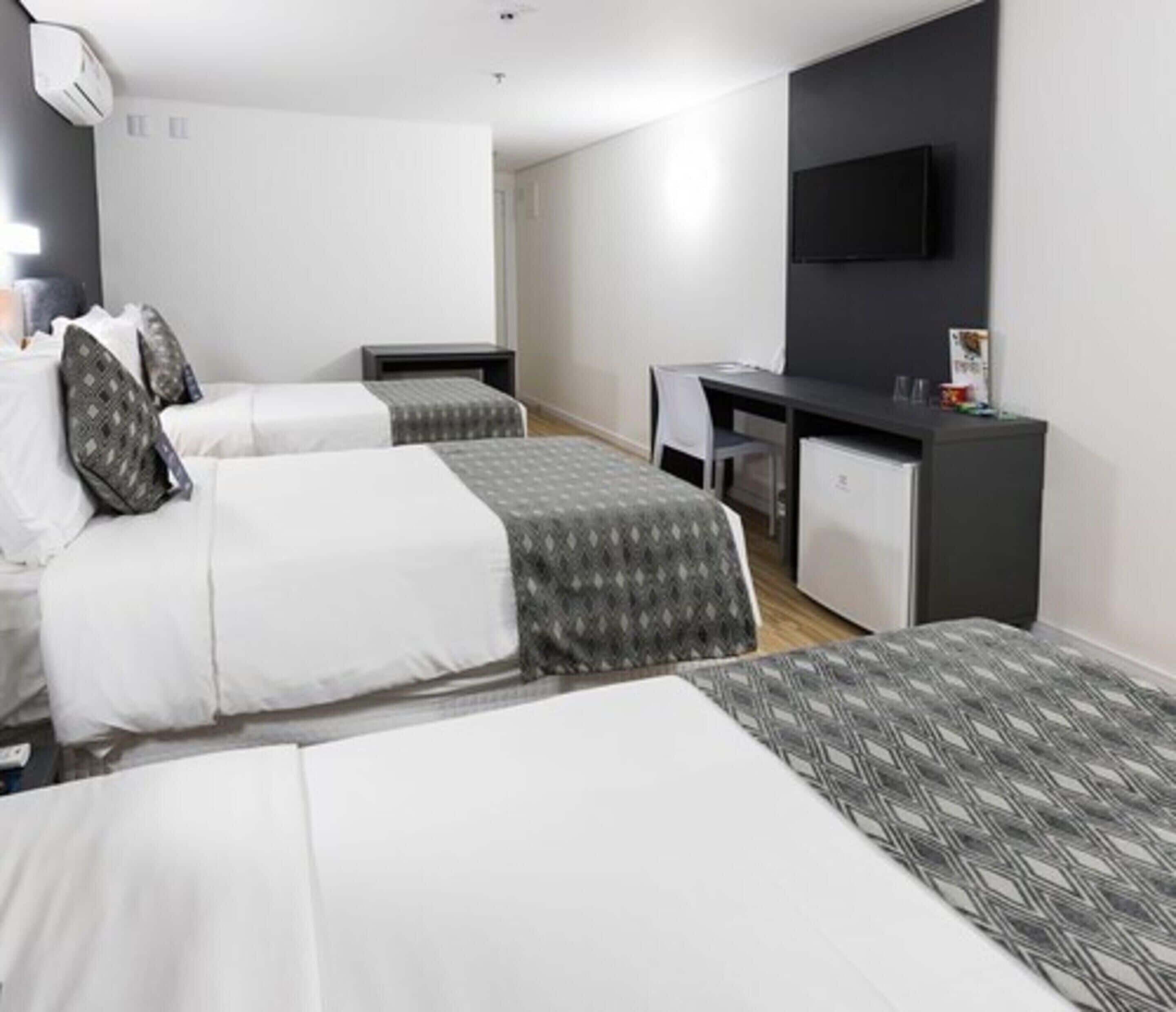 A hotel room with two beds, a desk, a chair, and a TV on the wall.