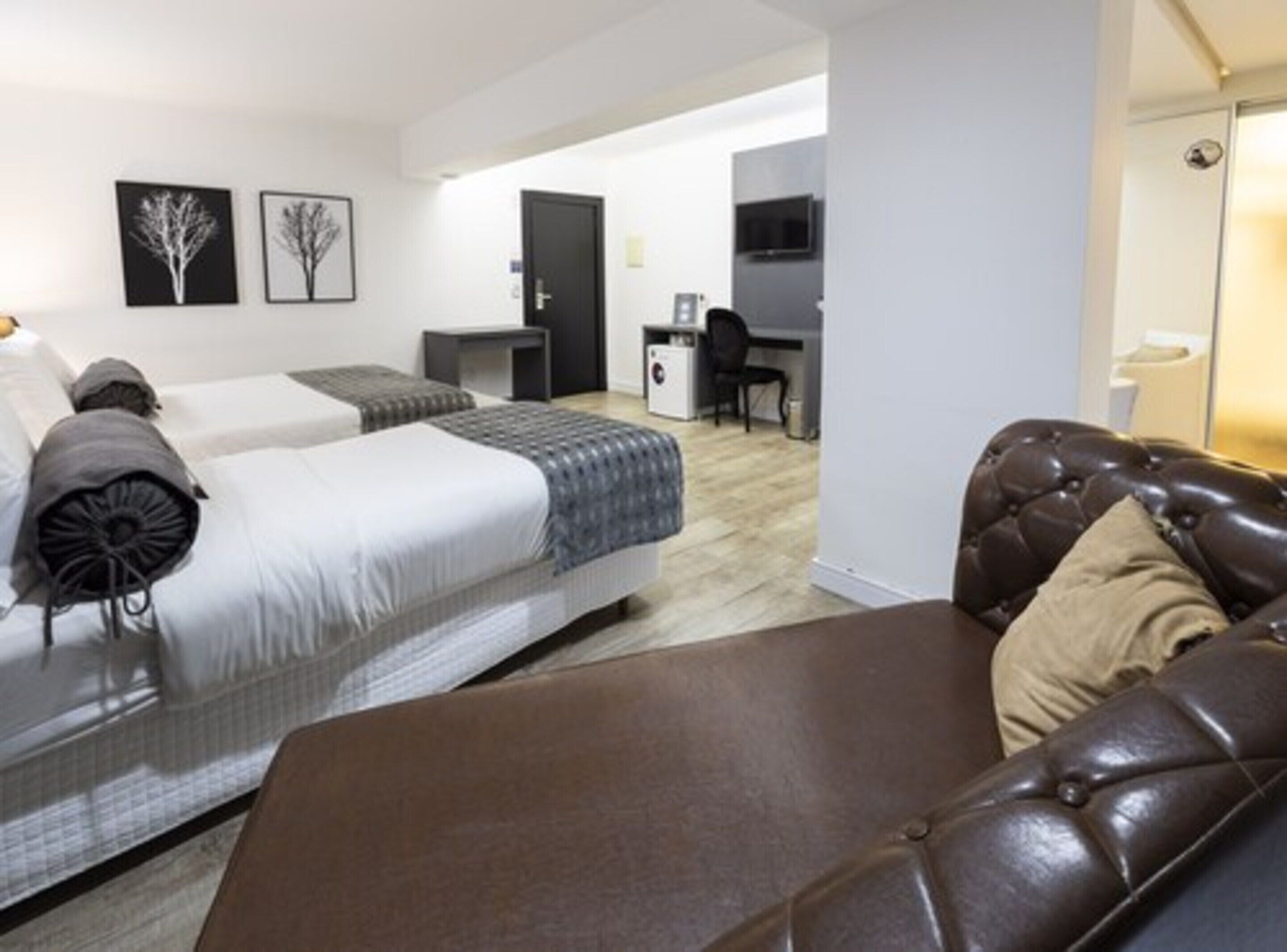 A modern hotel room with two beds, a desk, and a leather sofa.