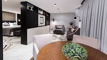 Una habitación de hotel moderna con una cama, una zona de estar con una mesa y sillas, un pequeño sofá y una planta en maceta.