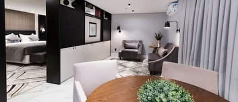A modern hotel room with a bed, a seating area with a table and chairs, a small sofa, and a potted plant.