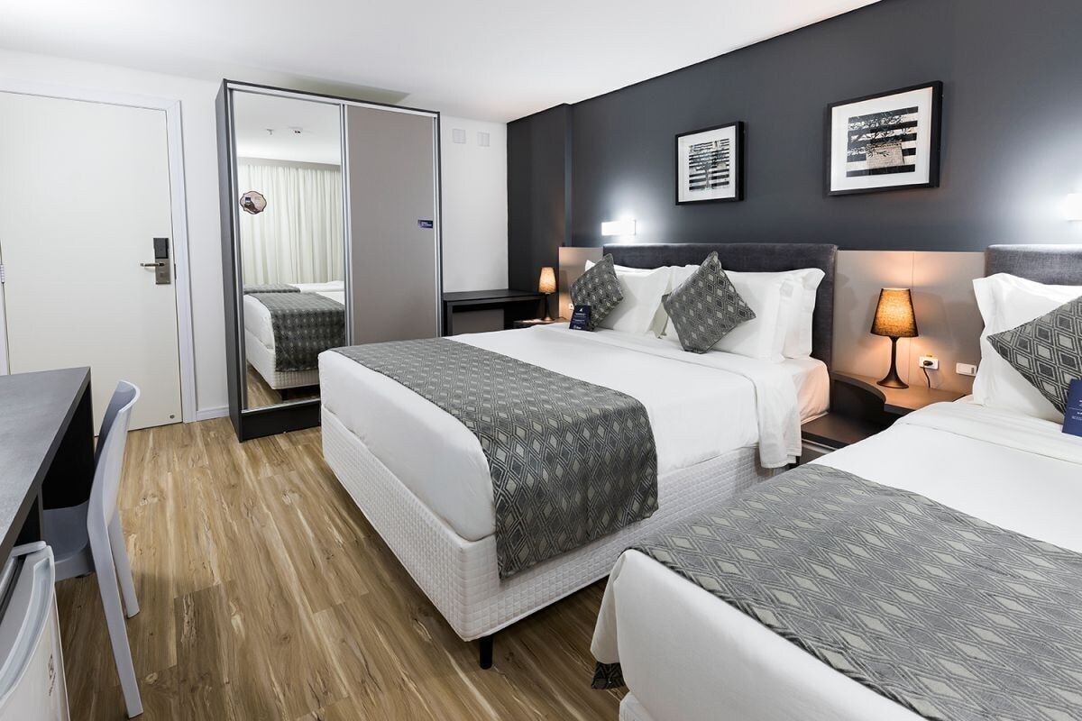 Una habitación de hotel con cama, mesitas de noche, escritorio y espejo.