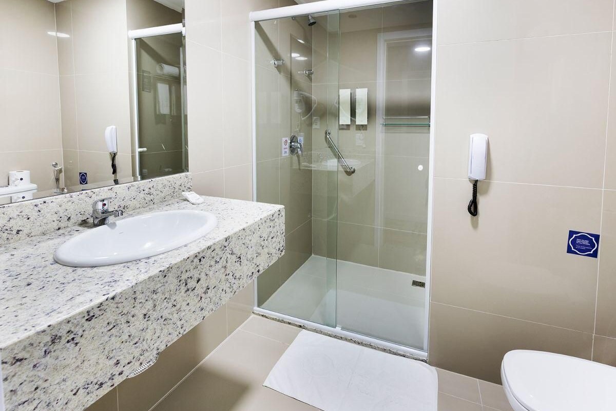 Un baño moderno con ducha envuelta en vidrio, un lavamanos con encimera de mármol y un inodoro.