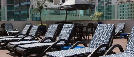 A rooftop lounge area with sun loungers and umbrellas, overlooking a cityscape.