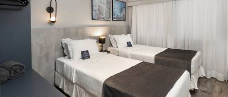 A hotel room with two beds, a desk, a lamp, and an air conditioner.