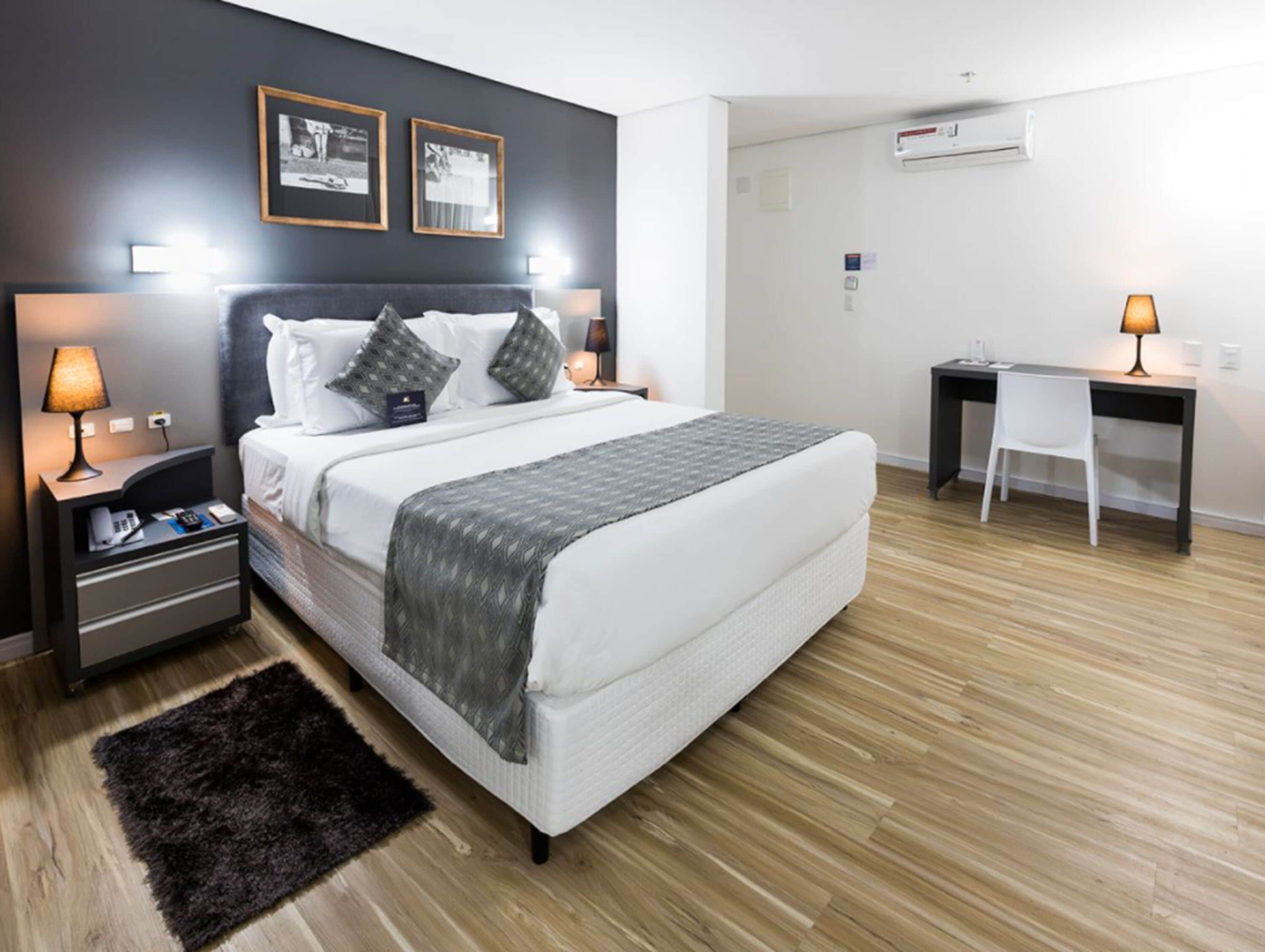Una camera d'albergo moderna con un letto grande, comodini con lampade, una scrivania e una sedia.