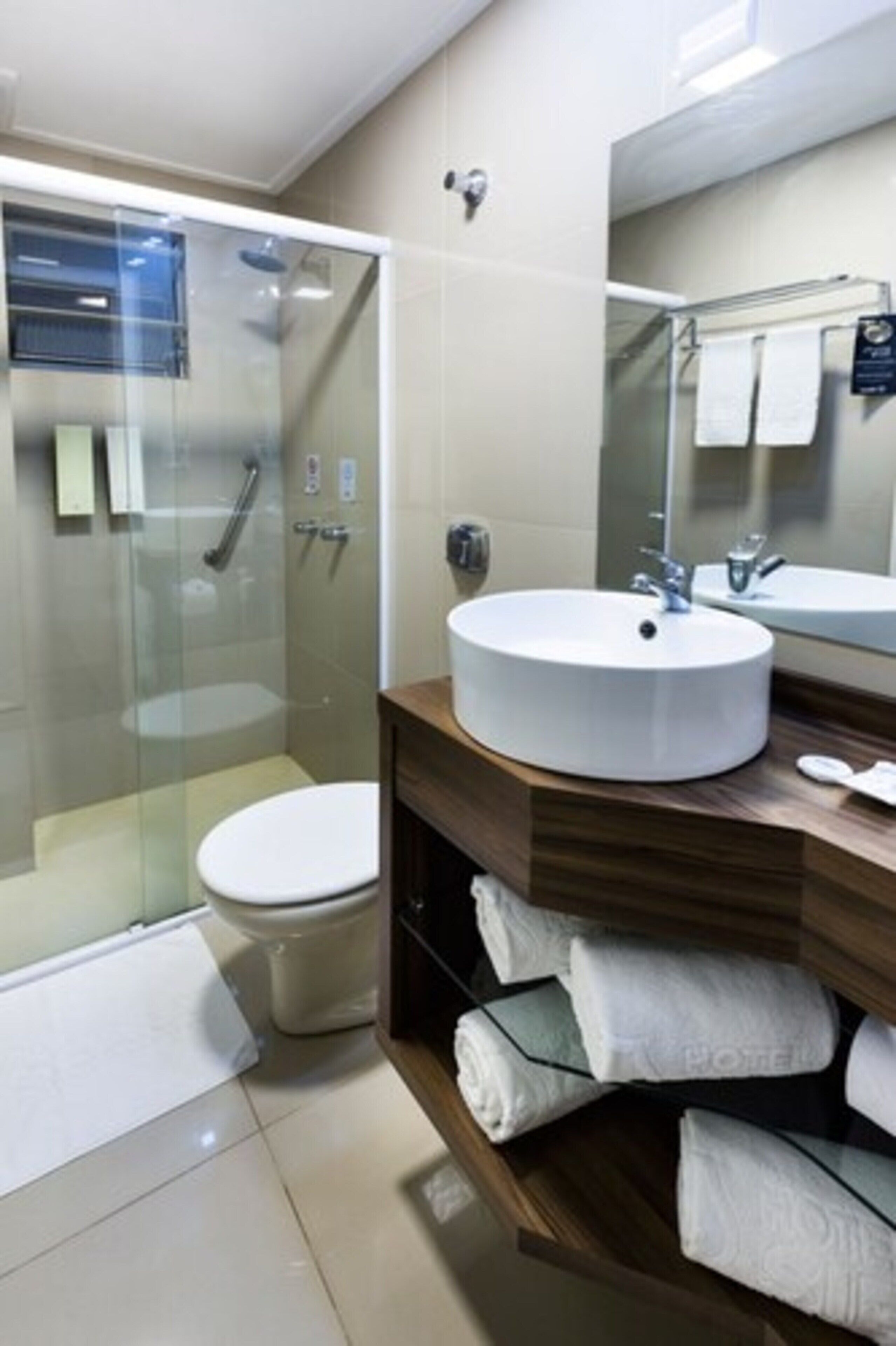 Un baño moderno con ducha envuelta en cristal, un lavabo redondo y un mueble de tocador de madera con toallas.