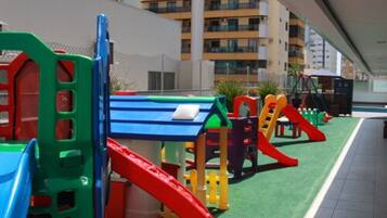A playground with colorful play structures, including slides and climbing frames, set against a backdrop of residential buildings.