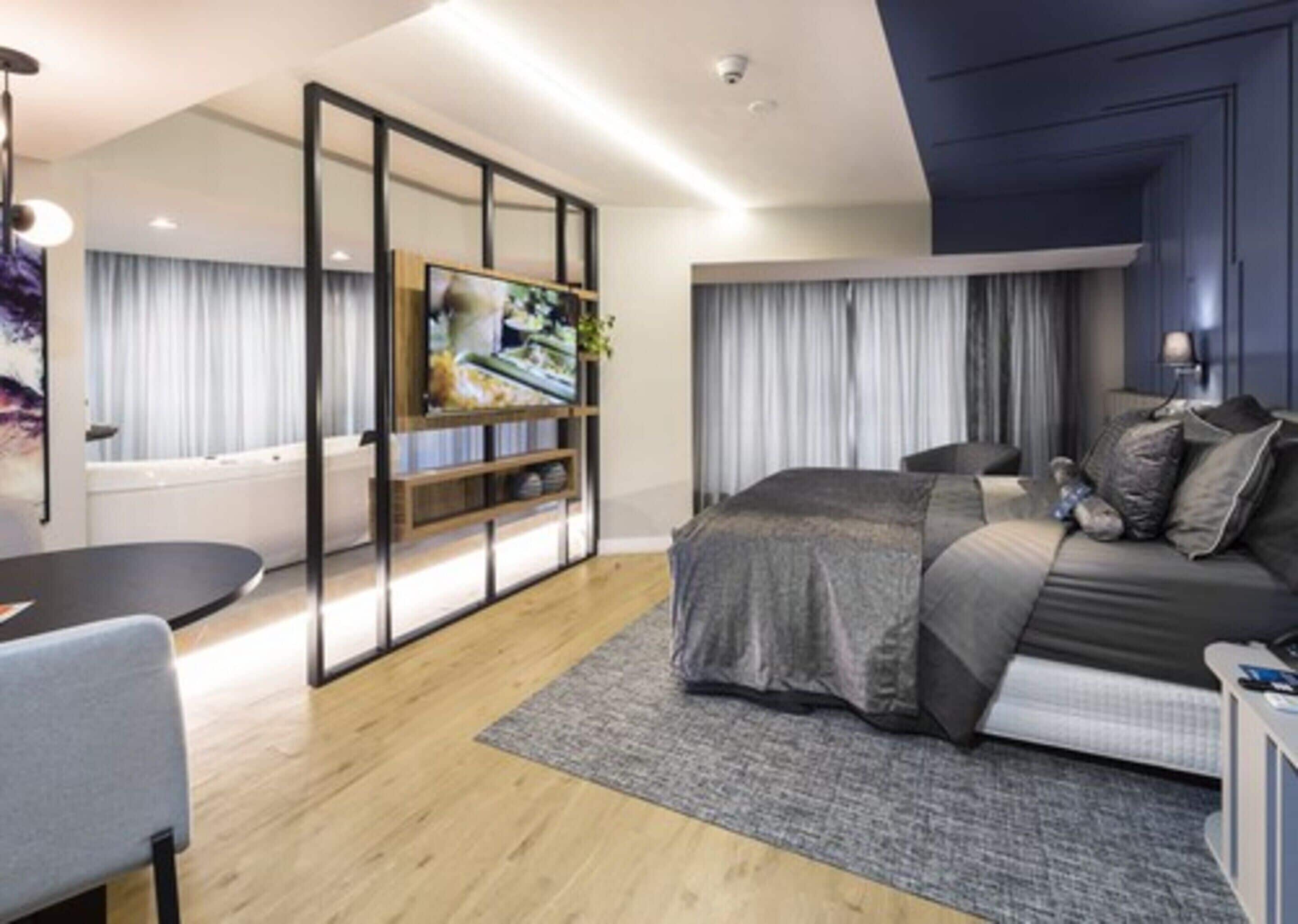Een moderne slaapkamer met een bed, een televisie, een bureau en een zithoek.