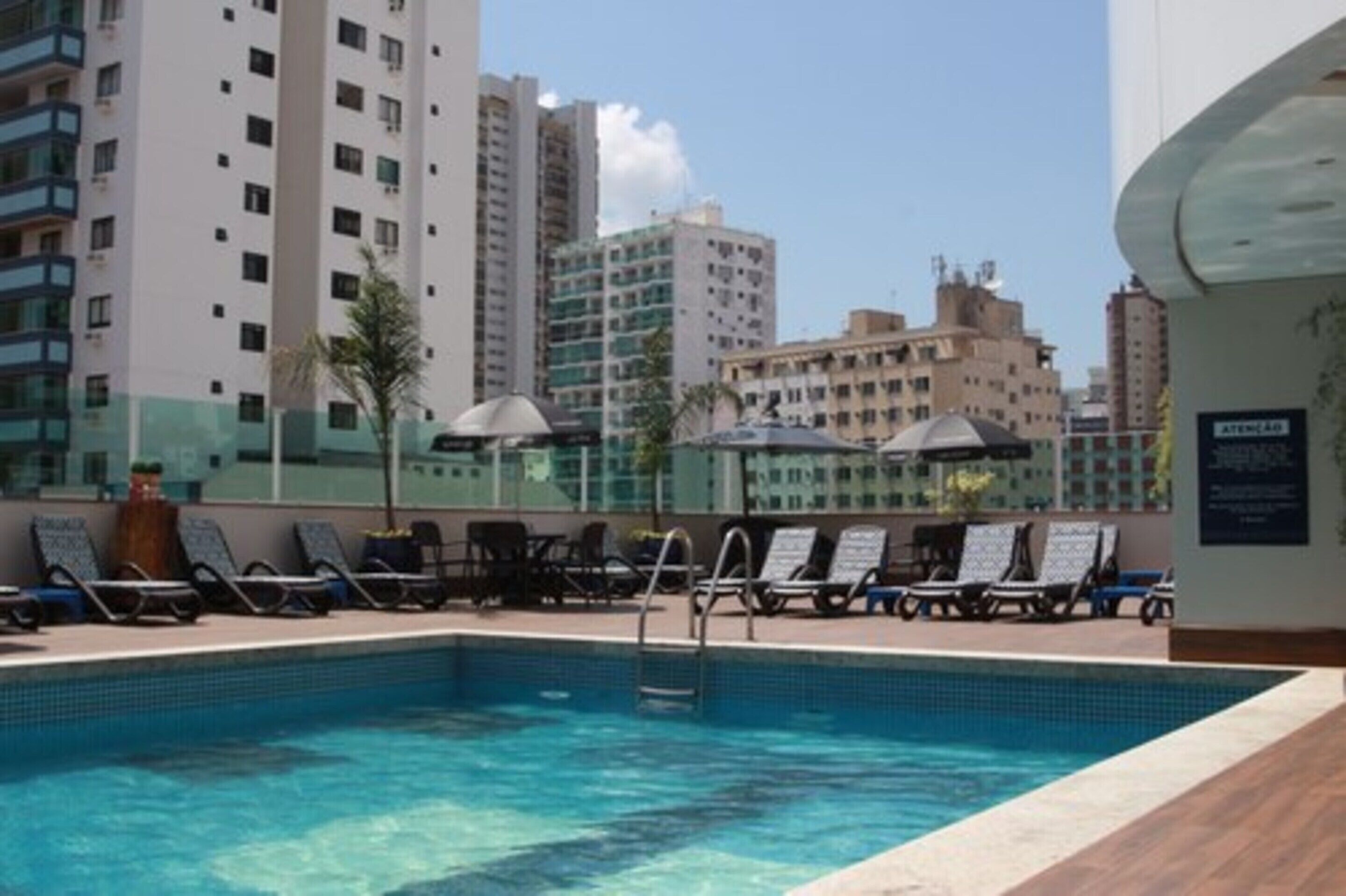 A rooftop pool with lounge chairs and umbrellas, surrounded by high-rise buildings.