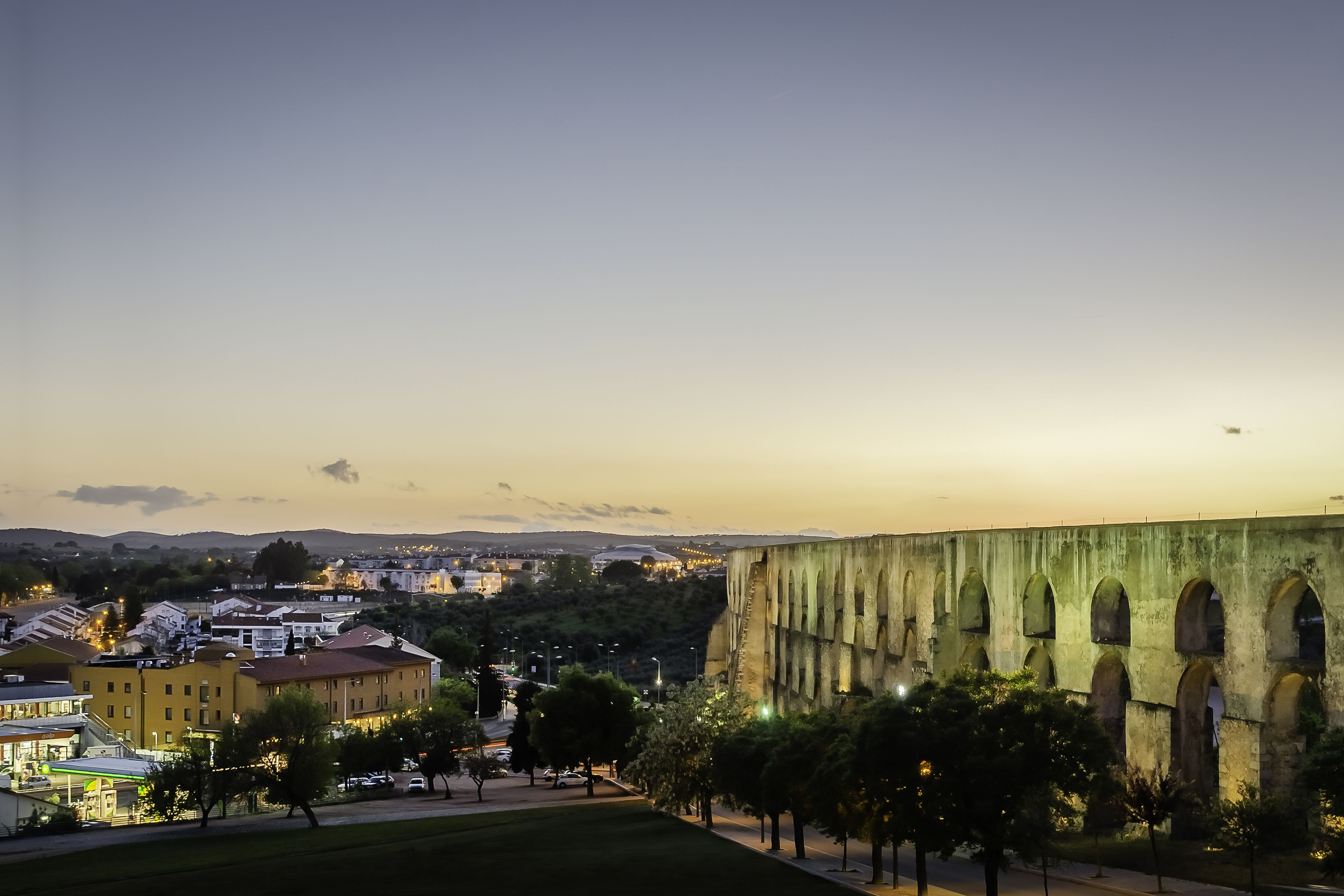 Un edificio grande con ventanas arqueadas y techo plano, rodeado de árboles y césped.