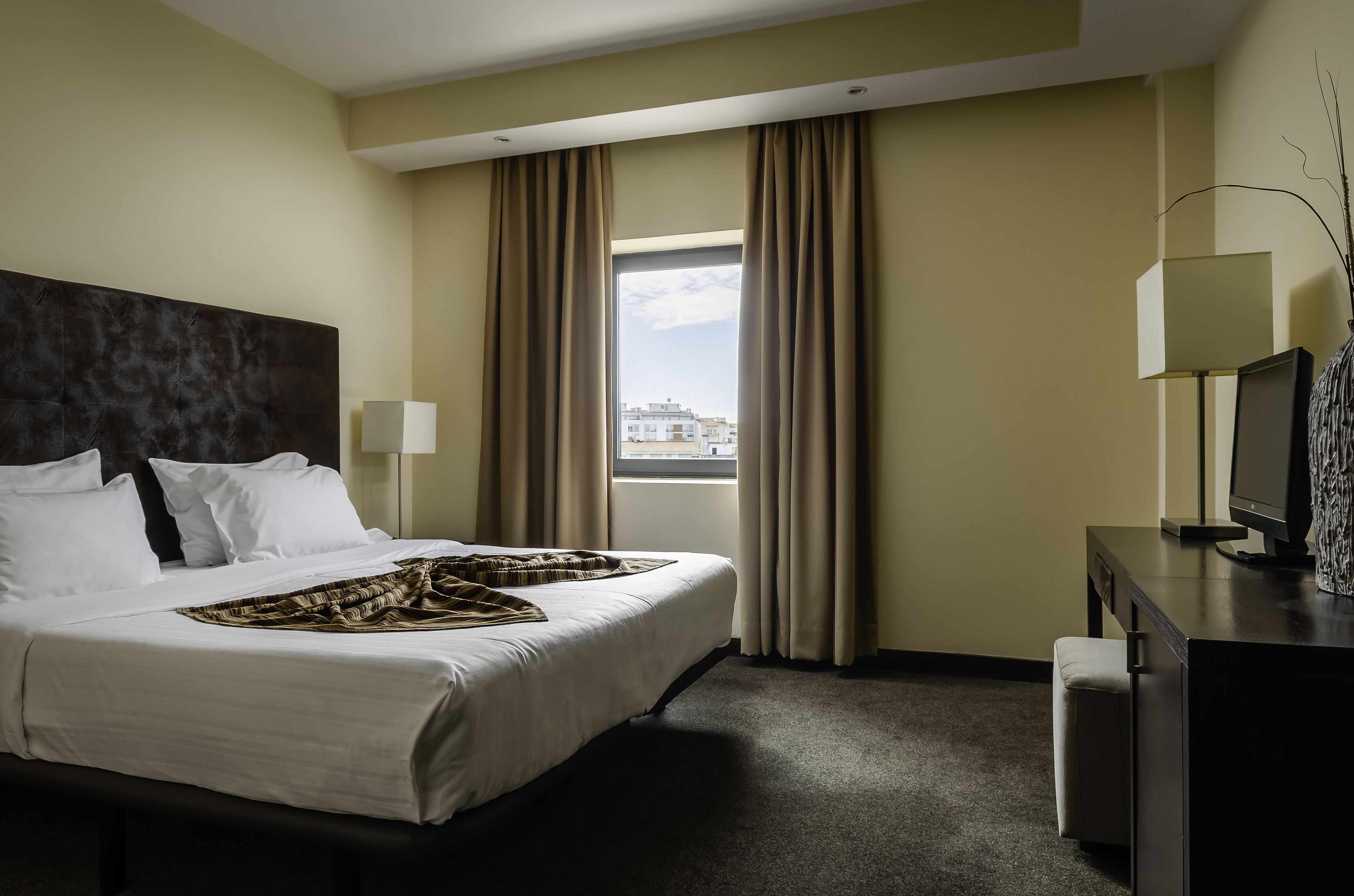 Habitación de hotel con una cama grande, un escritorio con computadora y una ventana con cortinas.