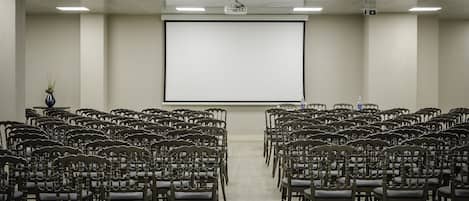Un salón de conferencias con filas de sillas de madera orientadas hacia una pantalla de proyección grande.