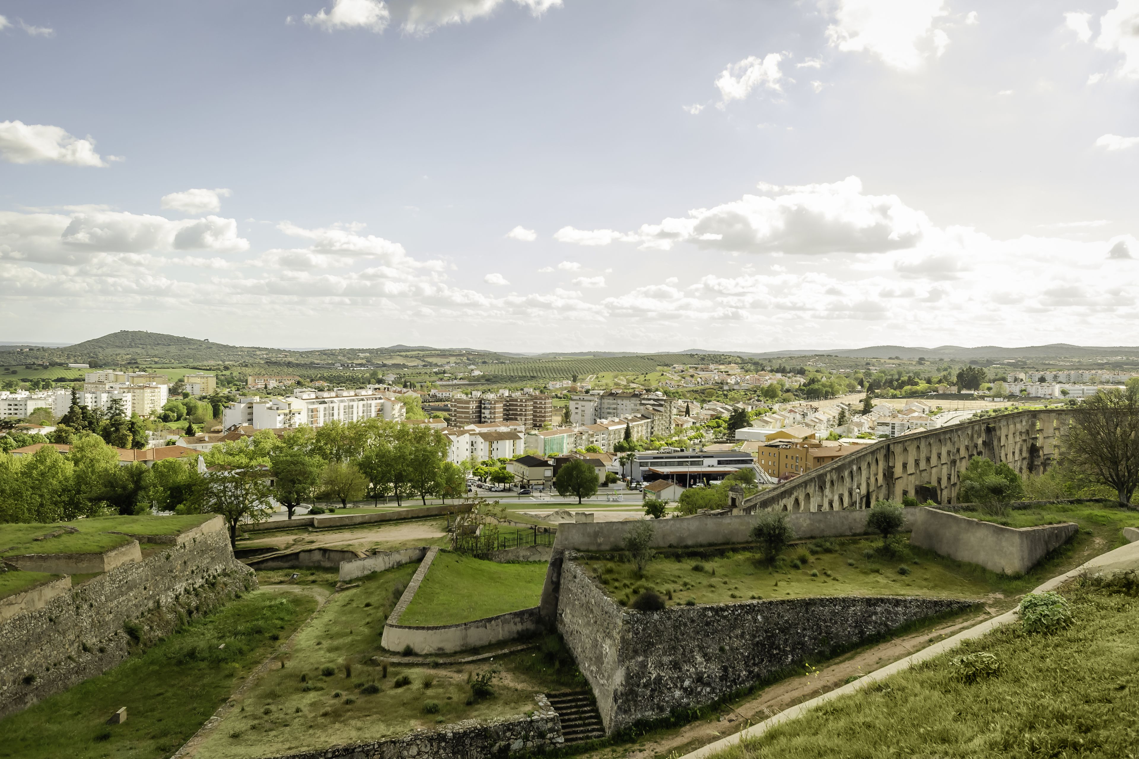 Un fort historique doté d’un mur de pierre, d’une zone herbeuse et offrant une vue sur un paysage urbain en arrière-plan.