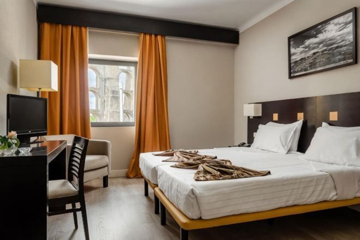 A hotel room with a bed, desk, chair, and a window with curtains.