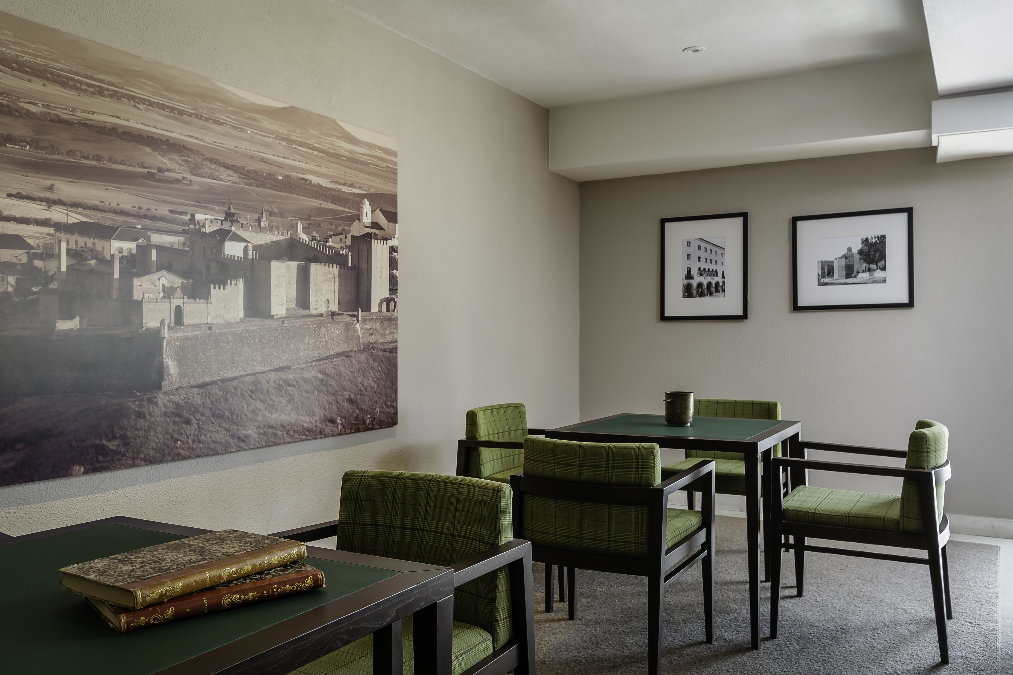 Un salón de conferencias con un cuadro grande, fotografías enmarcadas y sillas tapizadas de verde alrededor de una mesa.