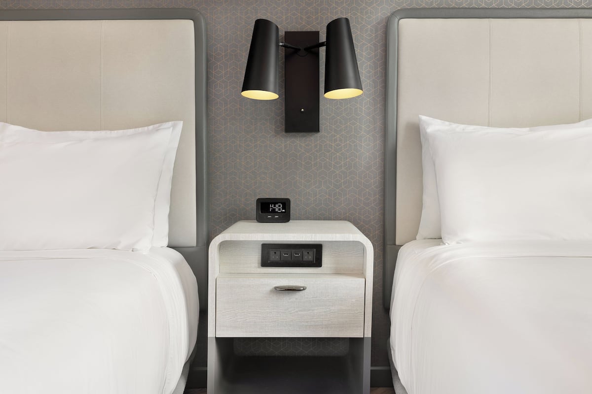 Una camera d'albergo con due letti, un comodino con una sveglia e lampade a parete.