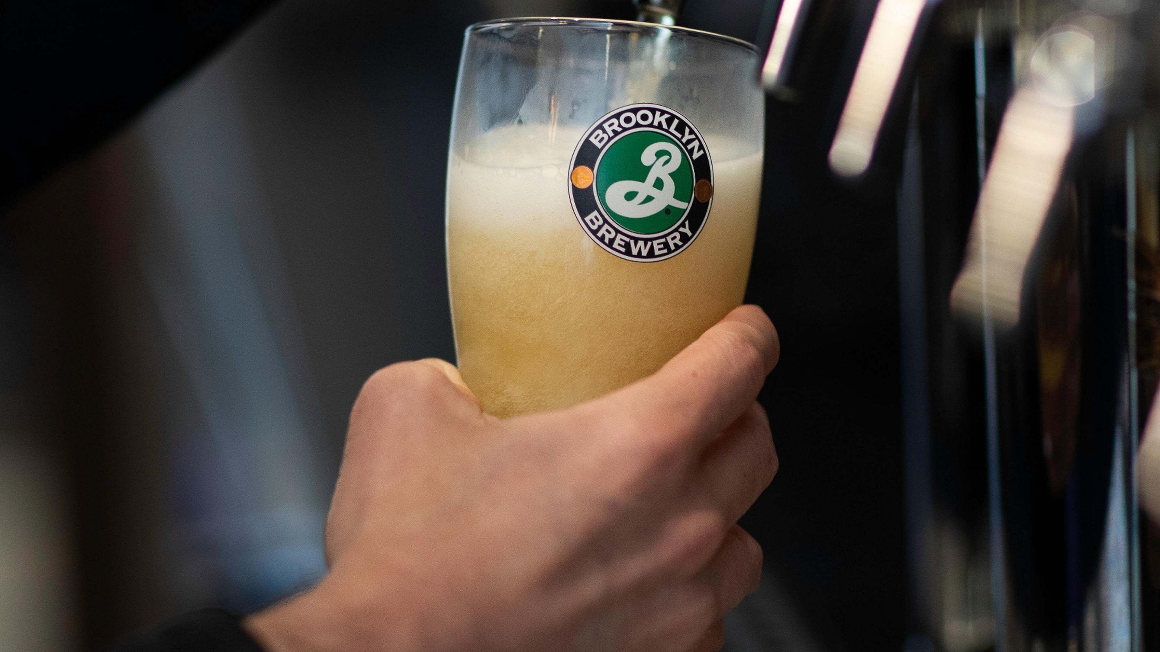 A hand holding a glass with a logo, likely in a bar or brewery setting.