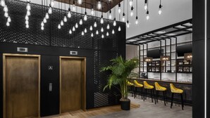 A modern lobby with two elevators, a bar area with yellow chairs, and a potted plant.