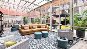 A spacious indoor area with a glass ceiling, a brown sofa, blue ottomans, and a patterned rug.