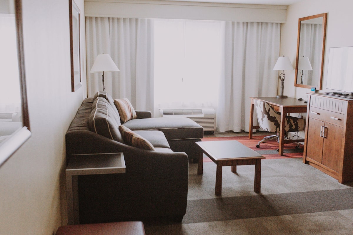 Une chambre d’hôtel comprenant un canapé, une petite table, un bureau avec une lampe, un miroir et un radiateur.