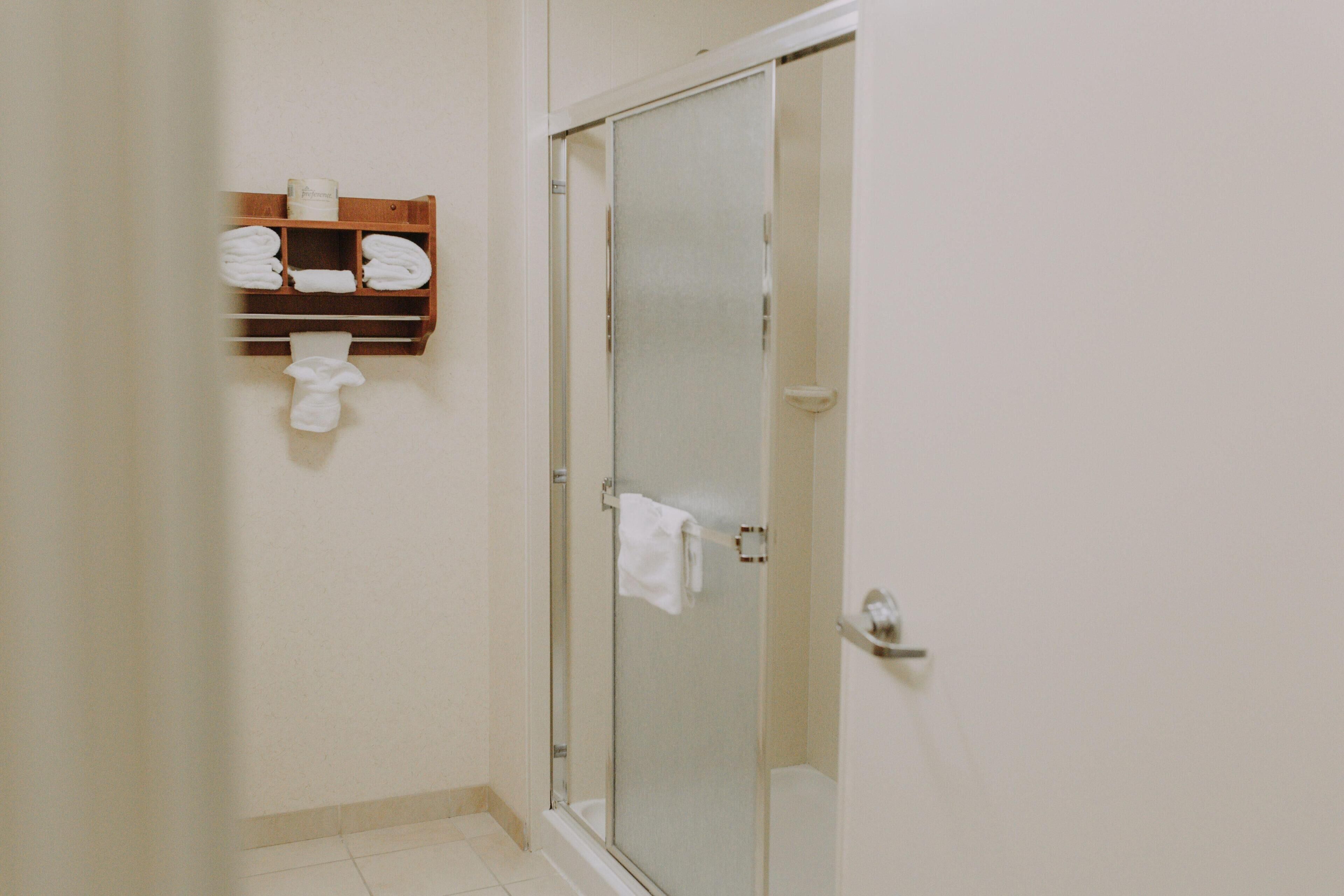 A bathroom with a glass shower door, a wooden towel rack with folded towels, and a white toilet.