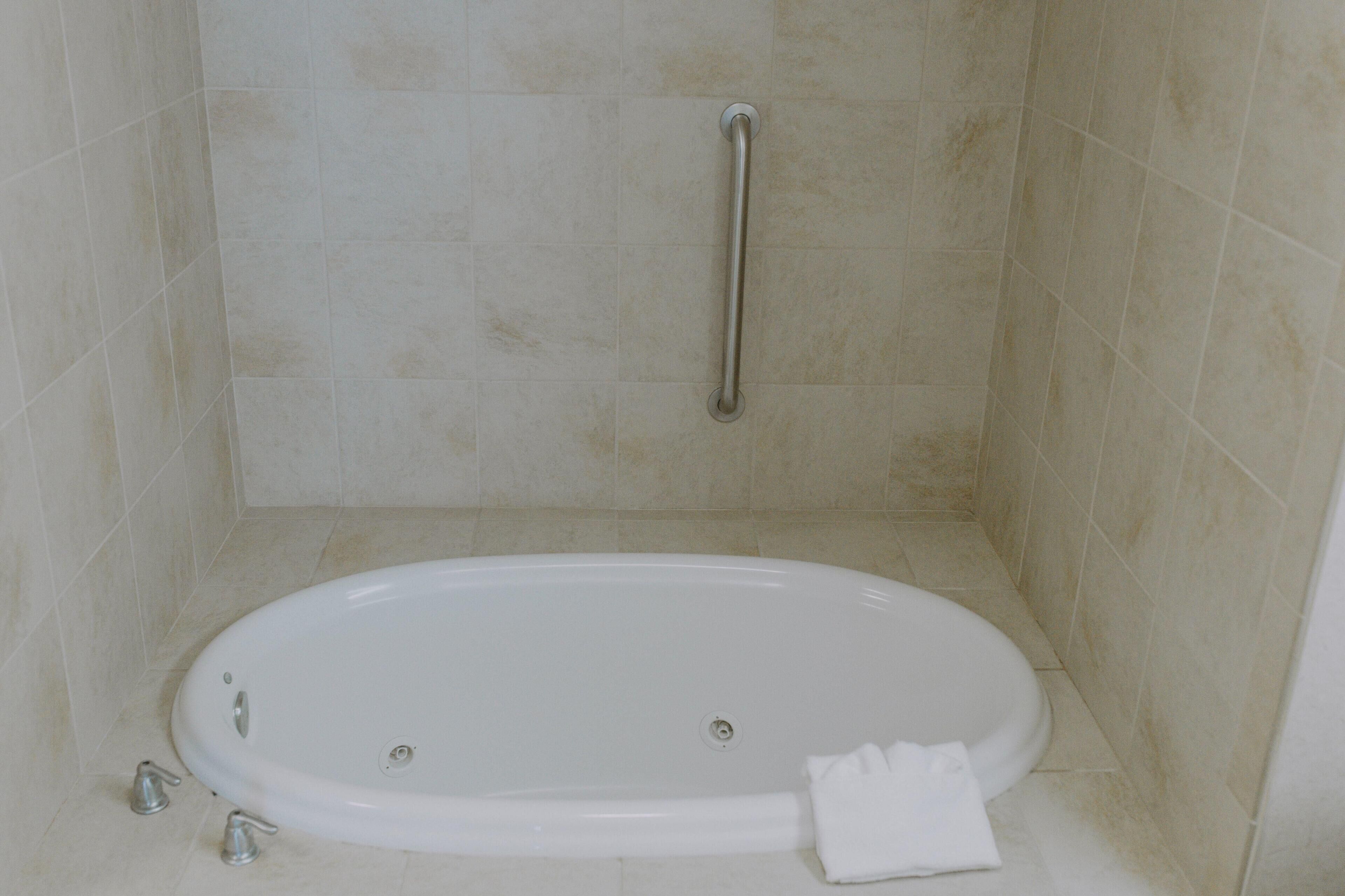 A bathroom with a bathtub, a handrail, and a towel on the floor.